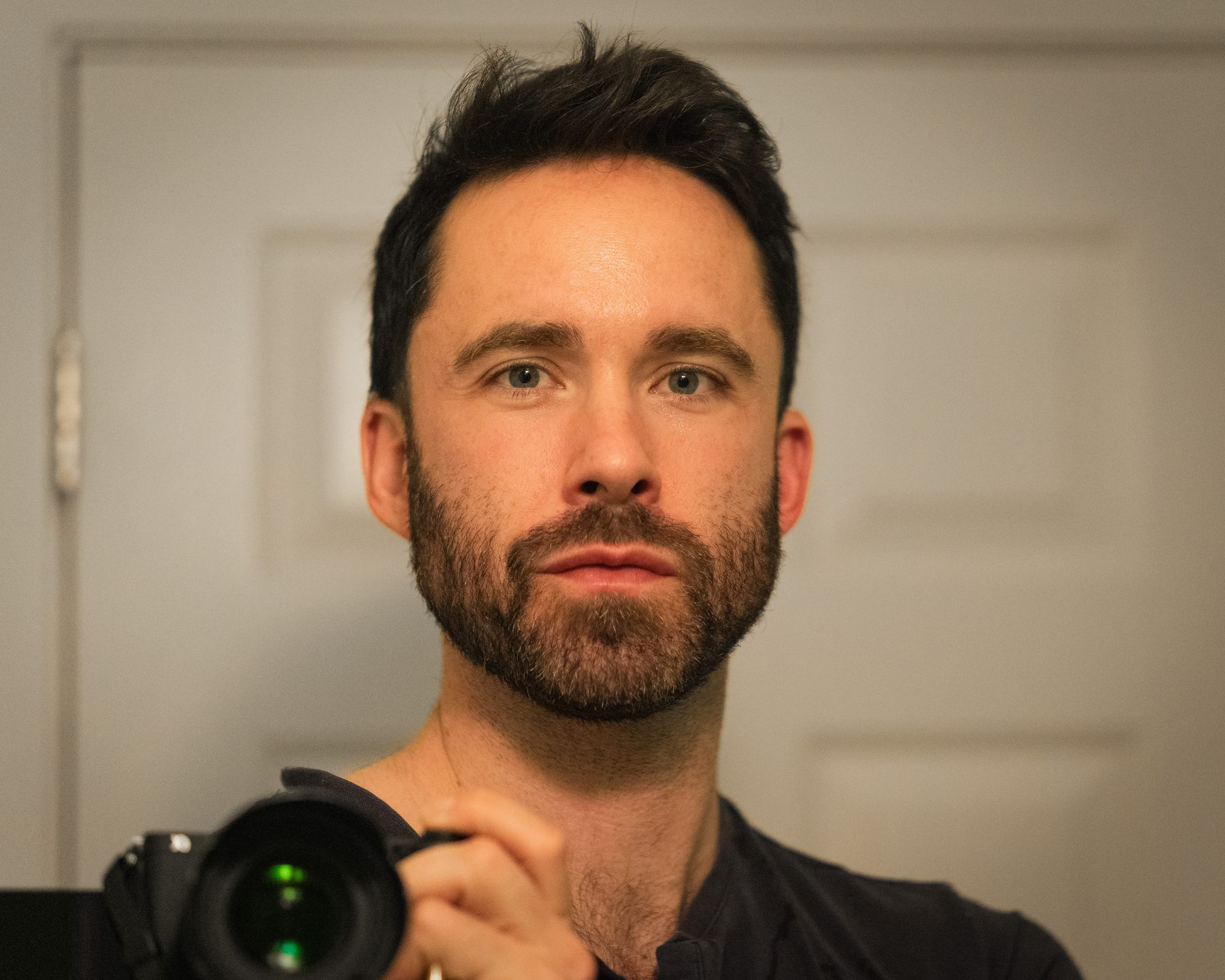 Self-portrait of Yaki holding a camera and looking directly into the mirror.