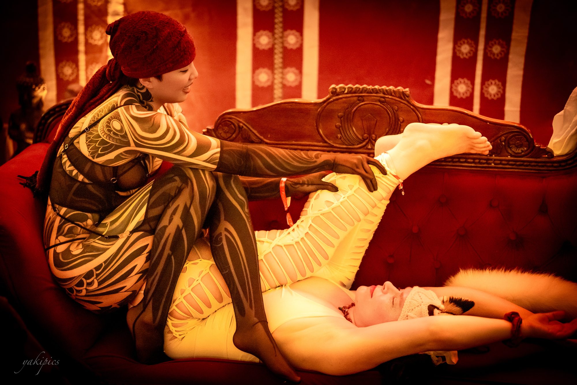 Two elaborately costumed people reclining together on a red couch.