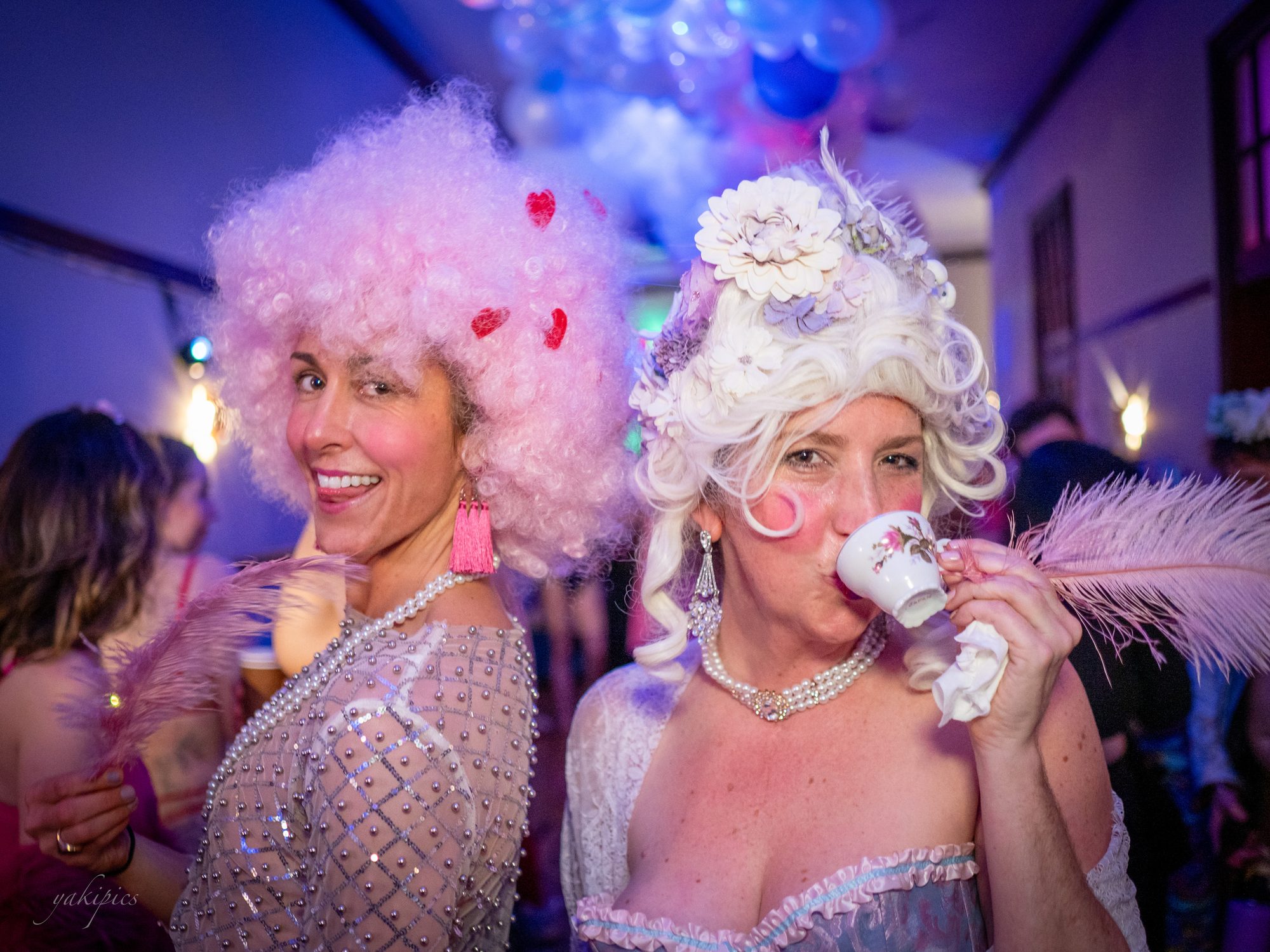 Two women in powdered wigs laughing together at a party.