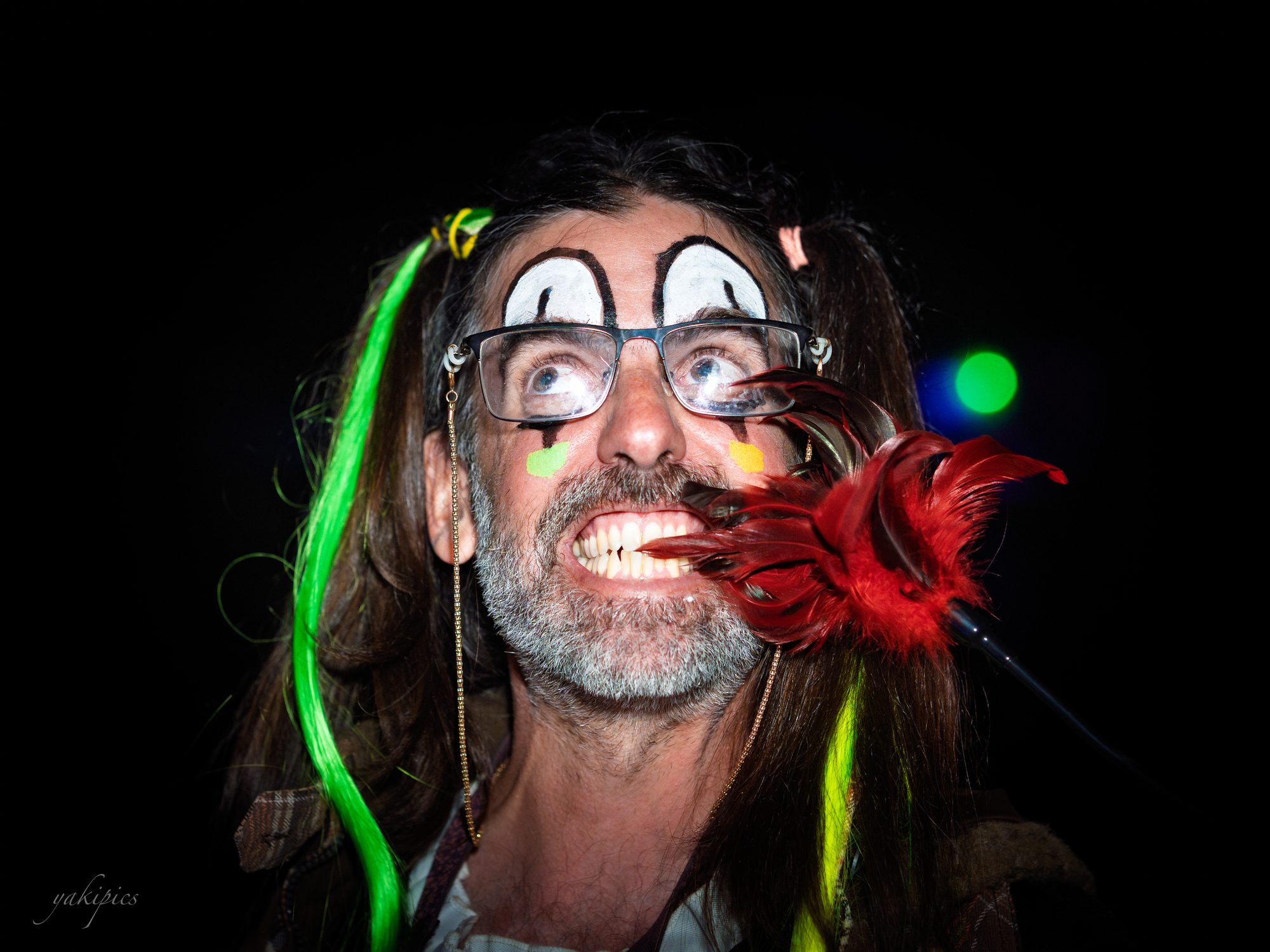 Costumed man with face paint, a bright feather, and an ecstatic upward gaze.