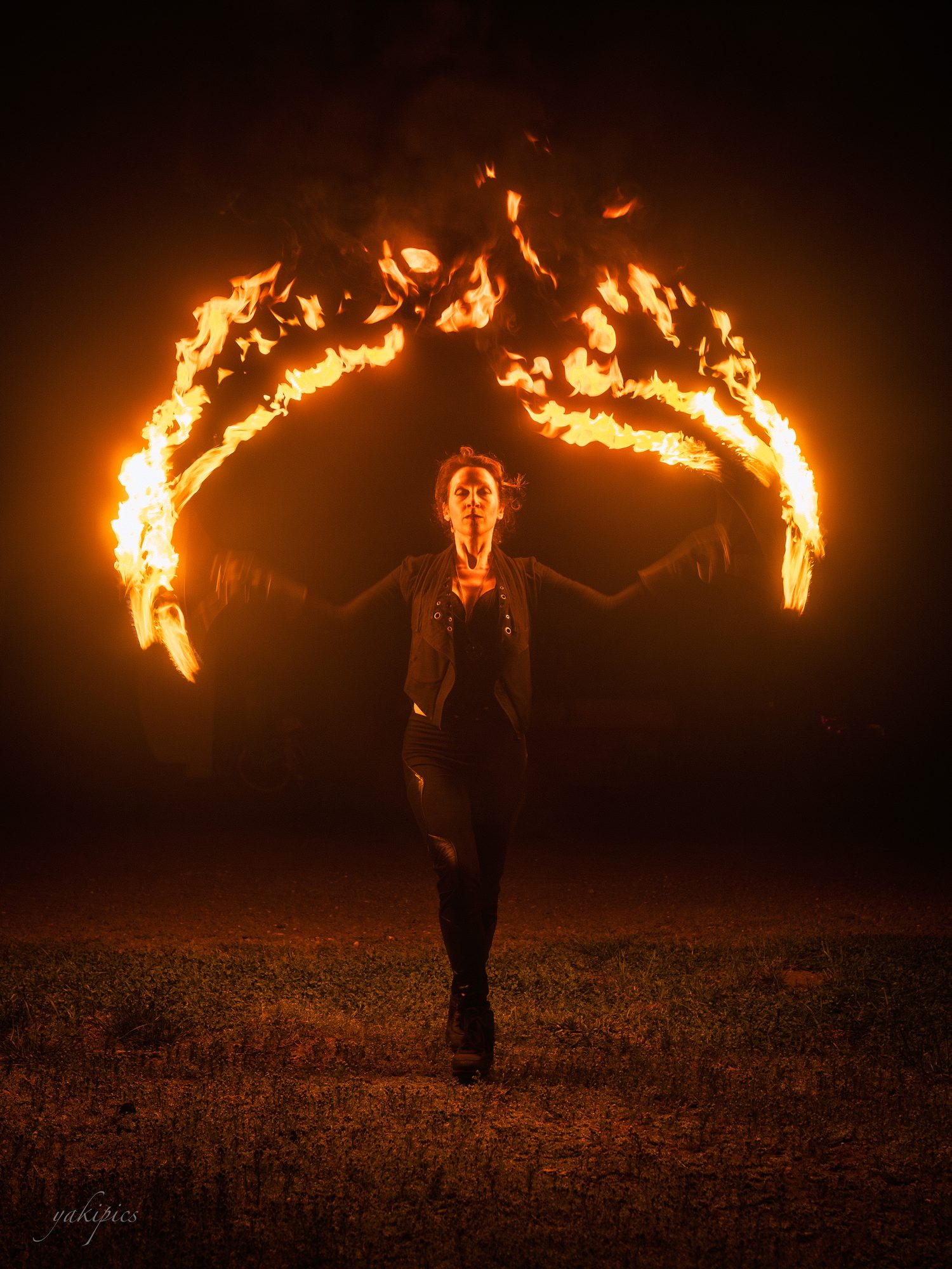Fire performer standing beneath two sweeping wings of flame in darkness.