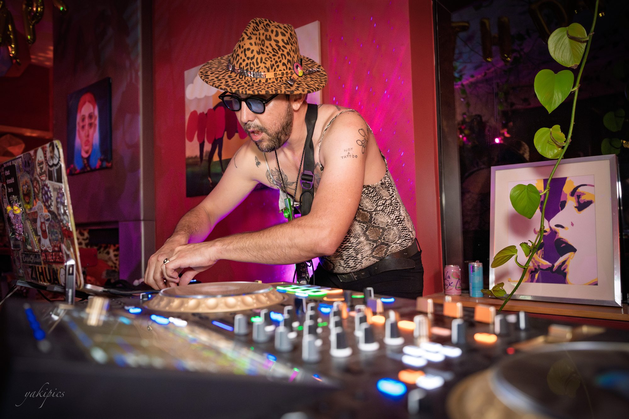 DJ absorbed in an illuminated mixing table surrounded by artwork.