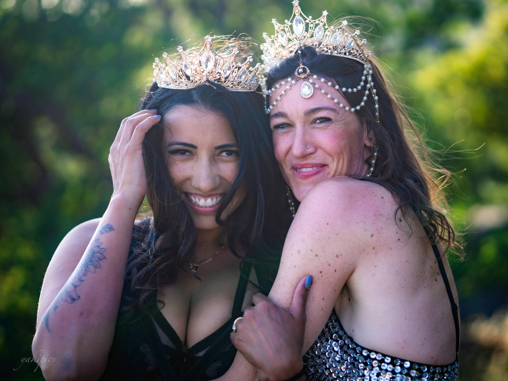 Two women wearing ornate crowns embracing in bright outdoor light.