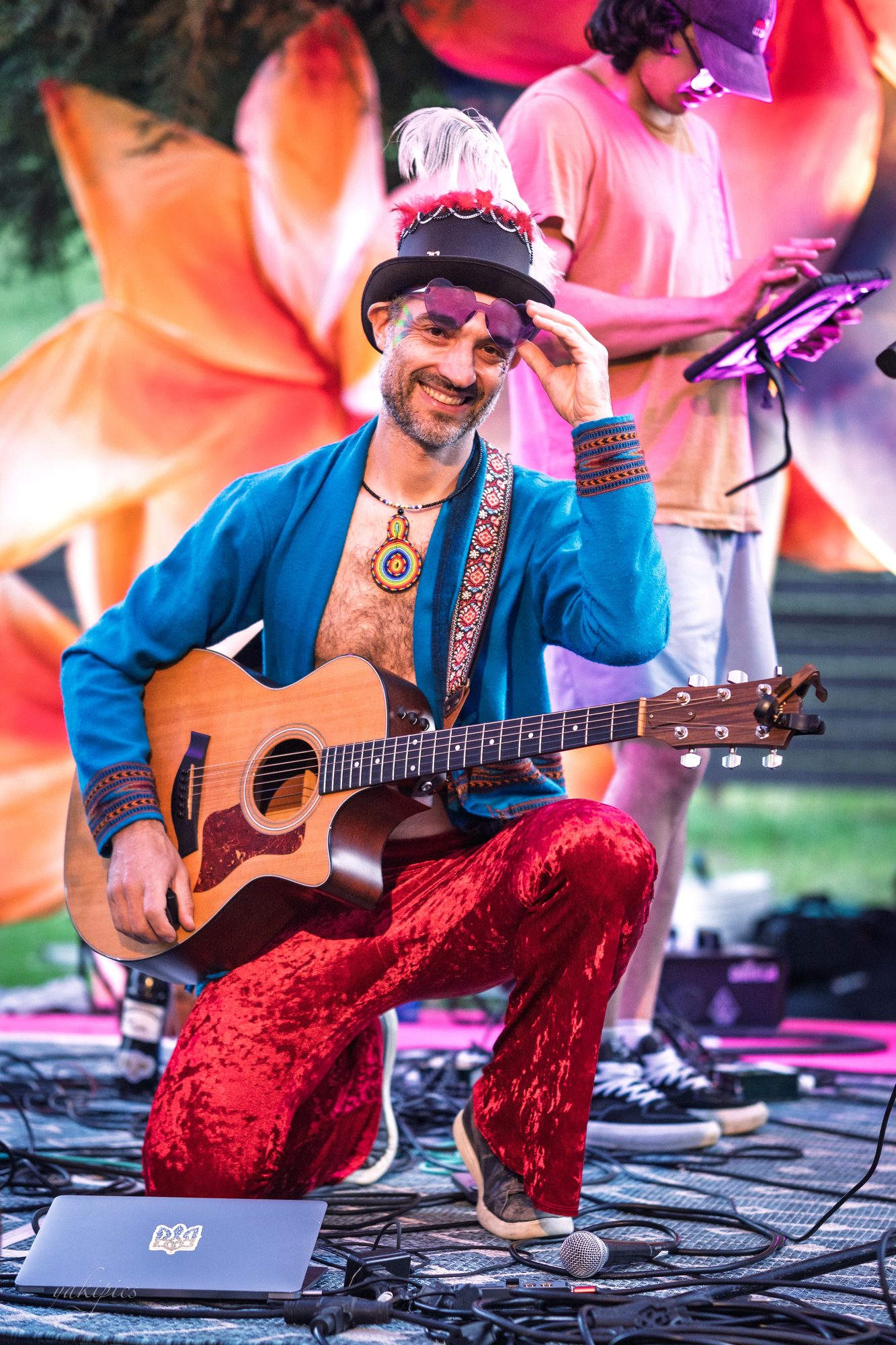 Guitarist kneeling in bright costume during an outdoor performance.