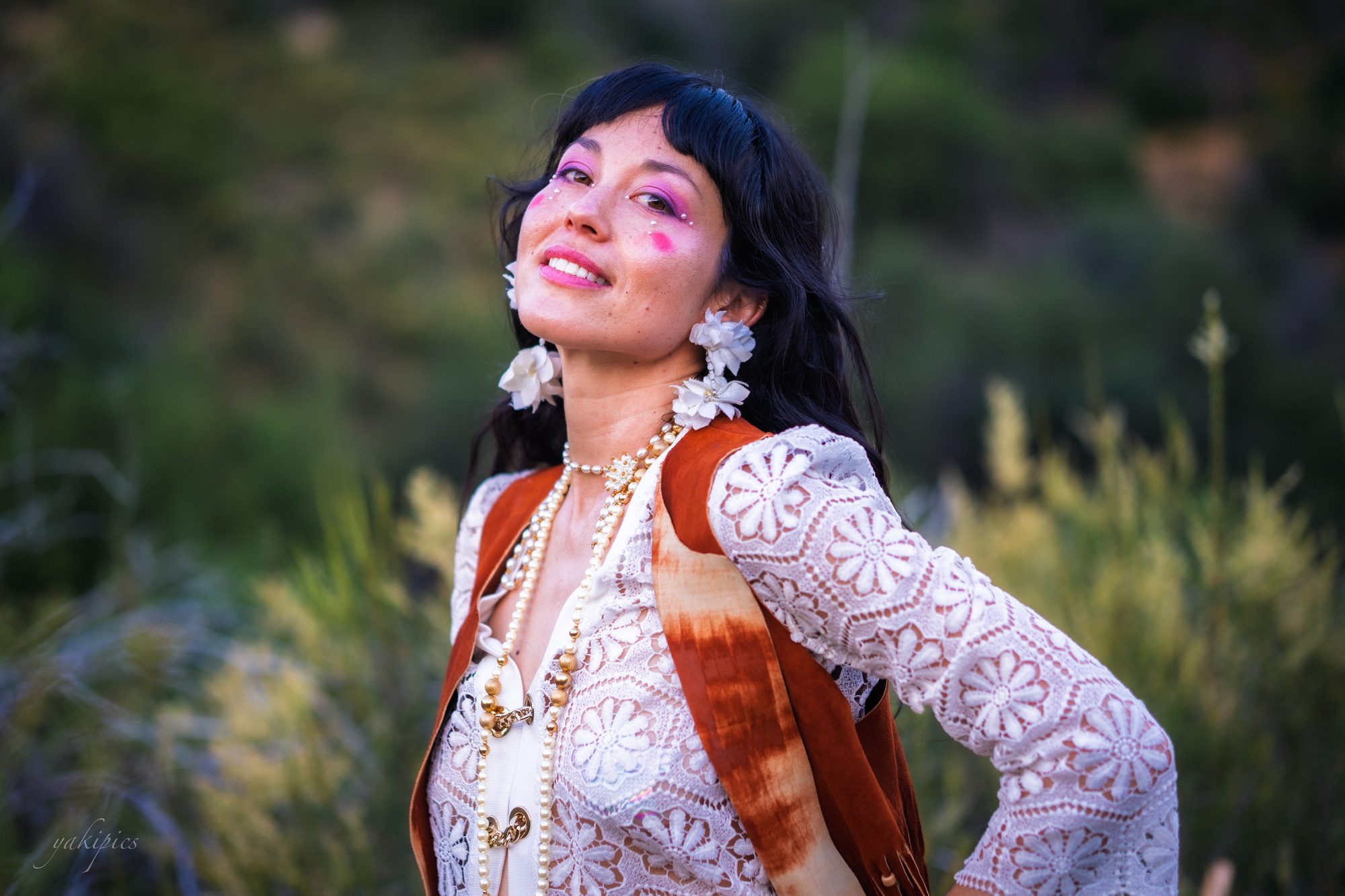 Woman in an ornate white-and-orange outfit standing among green brush.