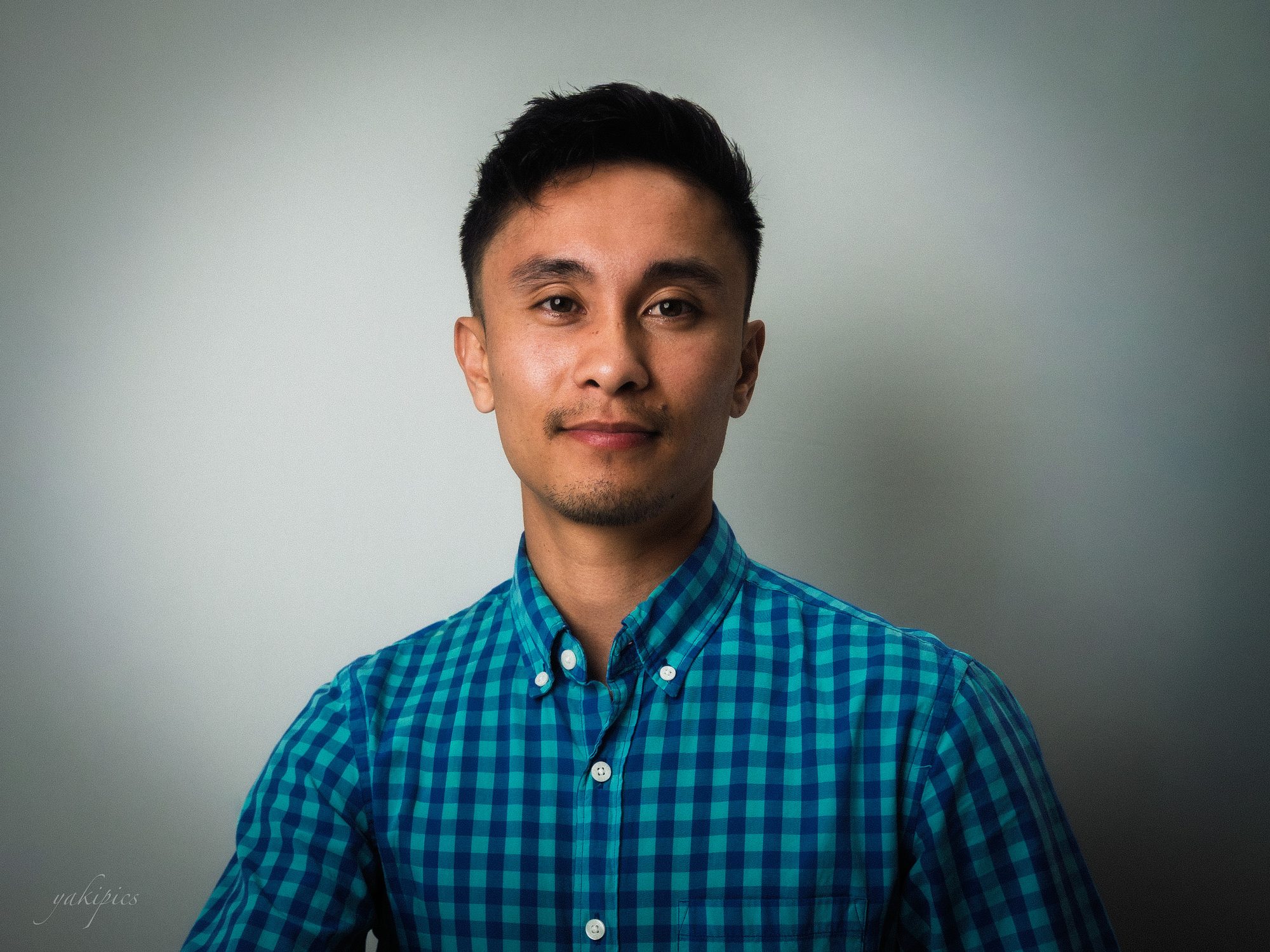 Studio portrait of a man wearing a blue checked shirt.