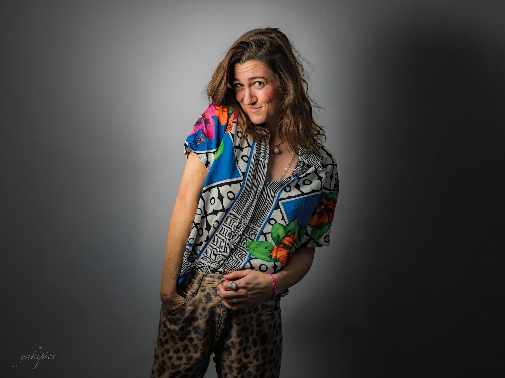 Woman in a patterned shirt giving a playful sideways expression against a gray studio backdrop.