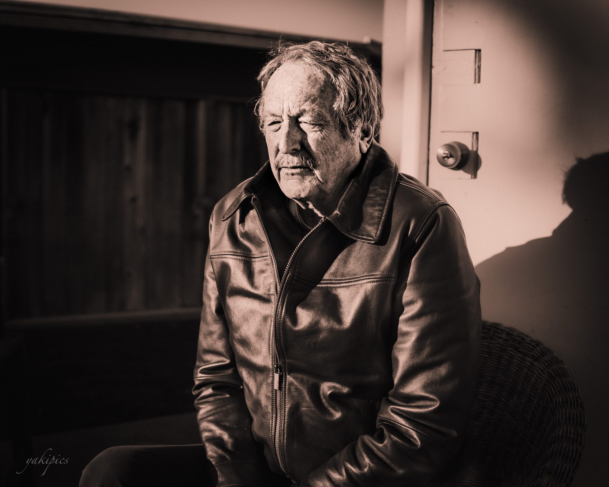 Black-and-white portrait of an older man in a leather jacket with his eyes closed.