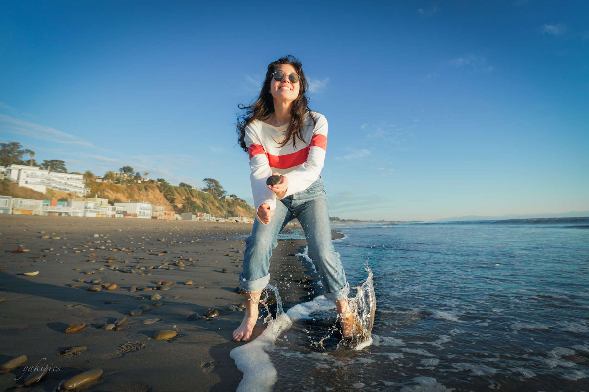 Woman splashing at the edge of the ocean beneath a wide blue sky.