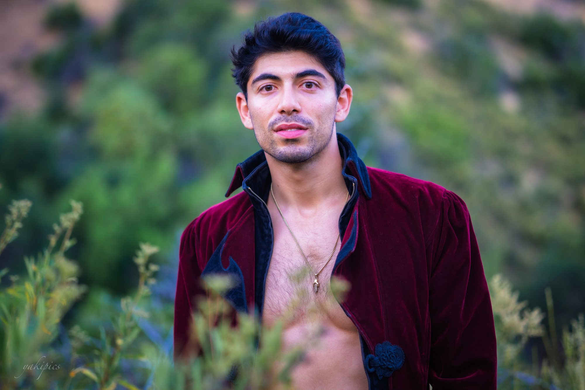 Man in a burgundy jacket standing among green plants.